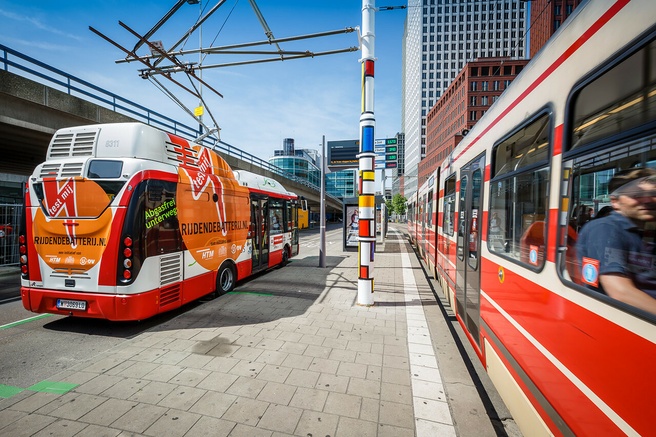 Een elektrische bus van HTM laadt aan de bovenleiding van een tram